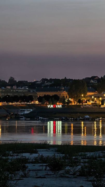 Evening lights of Vukovar reflected in the Danube, the illuminated VUKOVAR sign on the embankment