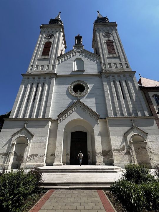 The façade of the Carmelite church in Sombor seen from the steps: two clock towers and a rose window