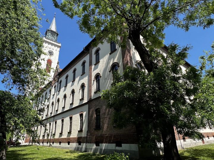 The long Carmelite monastery building in Sombor under acacia trees, a church tower behind