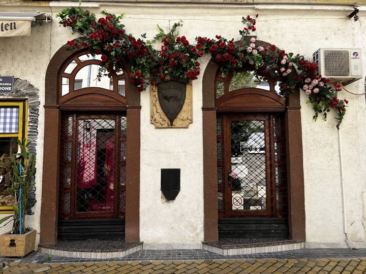 Two arched doors of a boutique in Sombor framed by red and pink roses, a shield with a lion between them